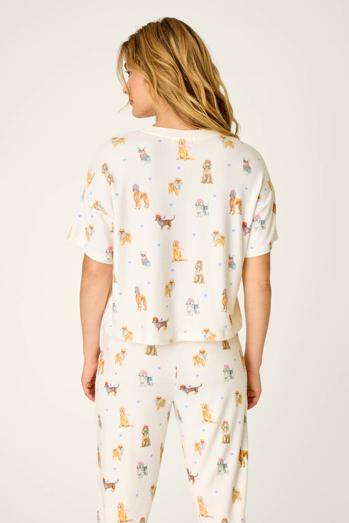 A woman with wavy blonde hair is shown from the back against a plain, light background, wearing the P.J. Salvage "Meet Me in Pawris Dog Print" Short Sleeve Top.