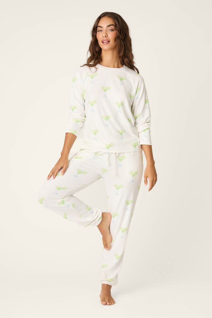 A woman stands barefoot on one leg against a plain light background, wearing the P.J. Salvage Margarita Mama Spicy Sips Long Sleeve Top in buttery-soft jersey with a fun margarita print.