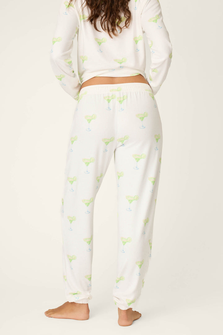 A person stands barefoot, facing away, in P.J. Salvage's Margarita Mama Spicy Sips Banded Pants with a playful green and blue margarita print, paired with a matching long-sleeve top.