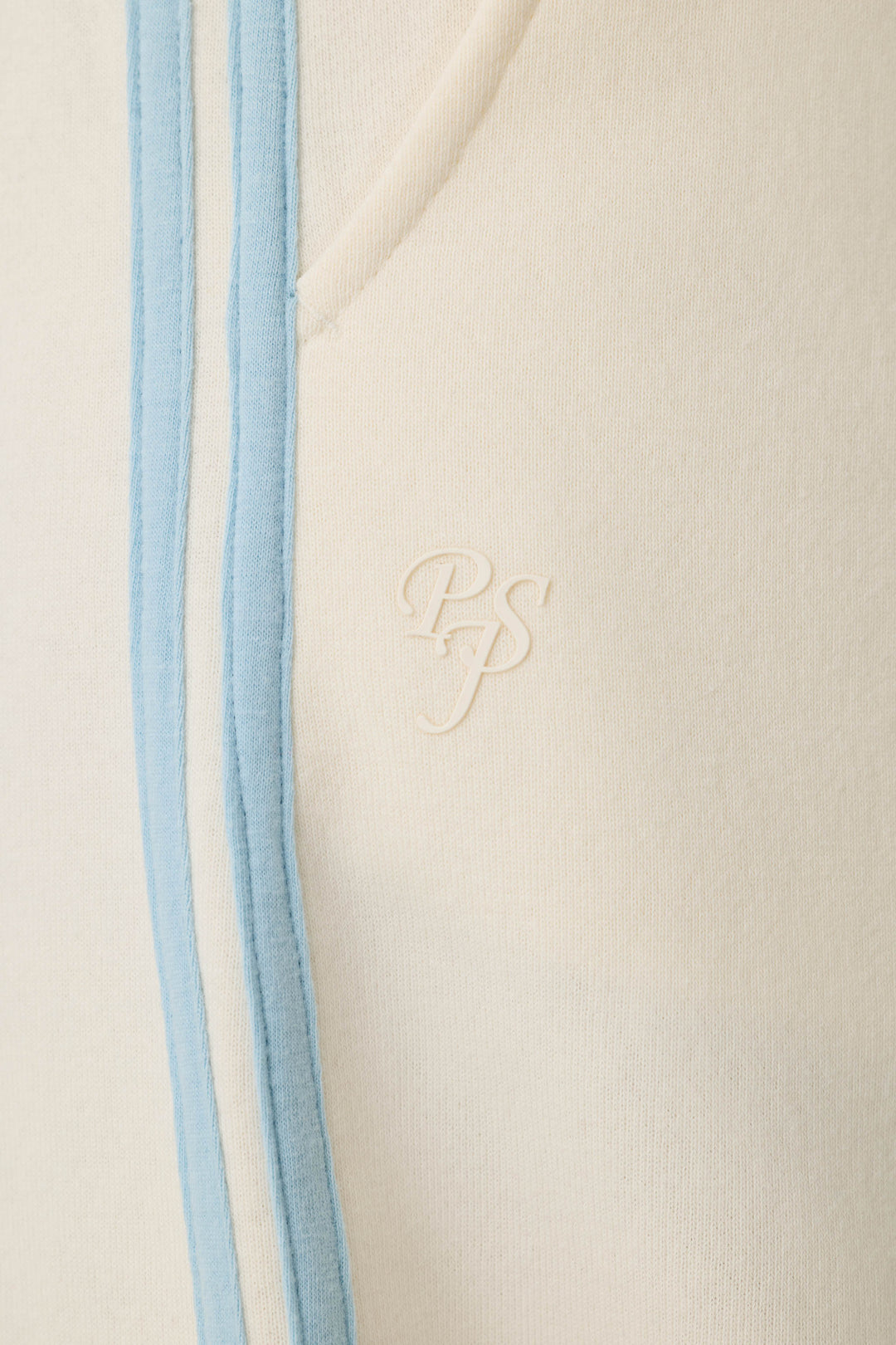 Close-up of the Nature Is My Therapy Adventure Awaits Good Hang Joggers by P.J. Salvage, featuring cream-colored fabric with light blue vertical stripes and an embossed PS logo. The soft texture resembles casual or athletic wear, with a visible seam and pocket edge.