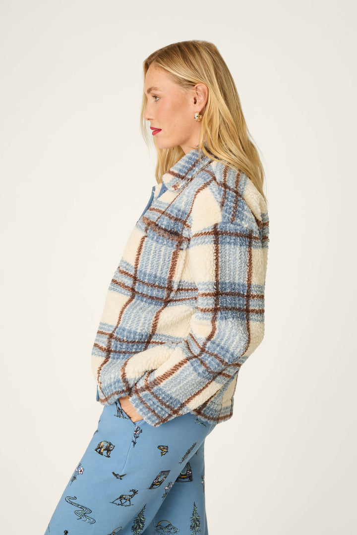 A person with long blonde hair stands in profile against a plain background wearing the P.J. Salvage Nature Is My Therapy Big Teddy Blue Plaid Sherpa Jacket paired with light blue pants featuring small printed designs.