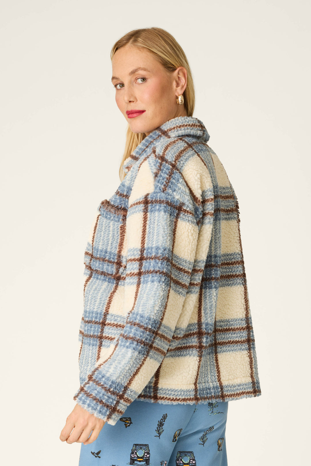 A woman wearing the P.J. Salvage “Nature Is My Therapy Big Teddy” blue plaid Sherpa jacket, paired with a patterned blue skirt, looks over her shoulder against a plain light background.