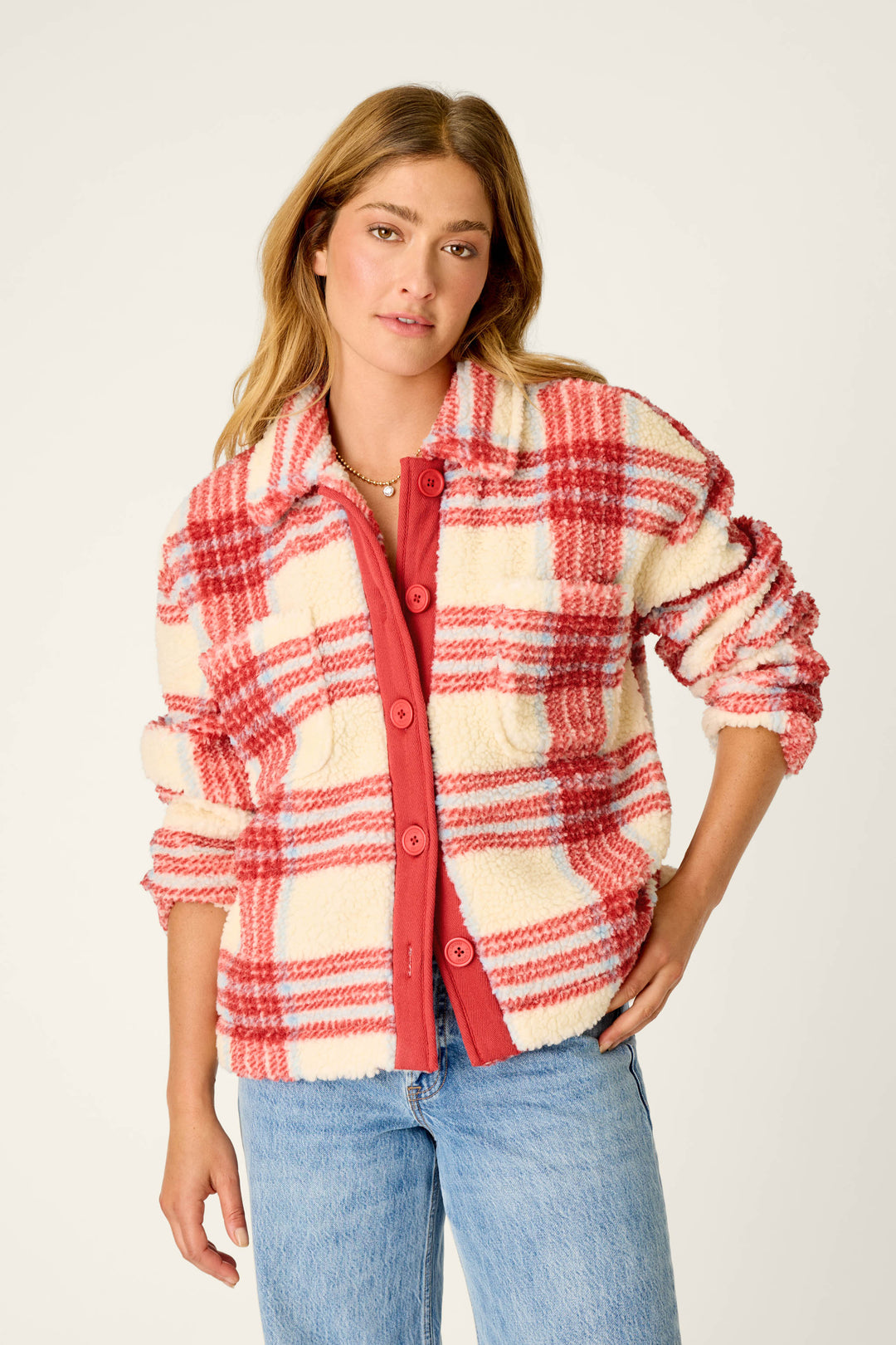 A woman stands against a plain background, looking at the camera with a neutral expression, wearing the P.J. Salvage Nature Is My Therapy Big Teddy Red Plaid Sherpa Jacket over a red shirt and blue jeans.