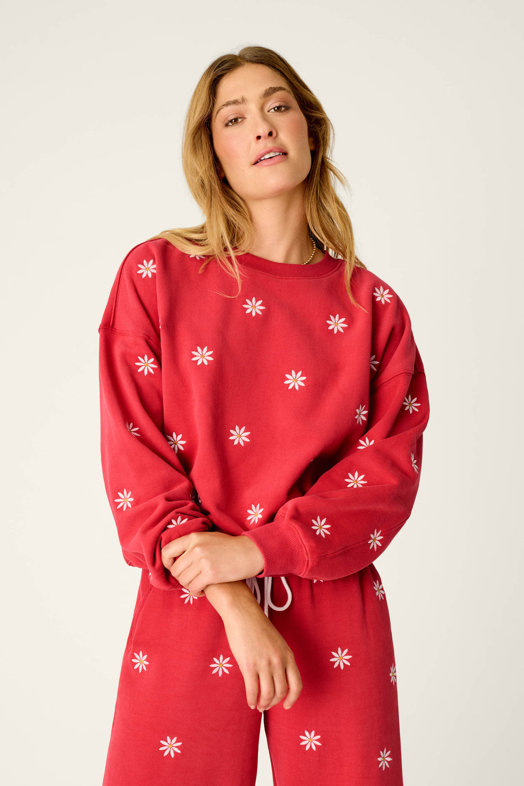 A woman stands against a plain light background, looking at the camera with a relaxed expression while wearing the P.J. Salvage “Nature Is My Therapy Embroidered Flowers Frankie Sweatshirt” in matching red with small white flower patterns.