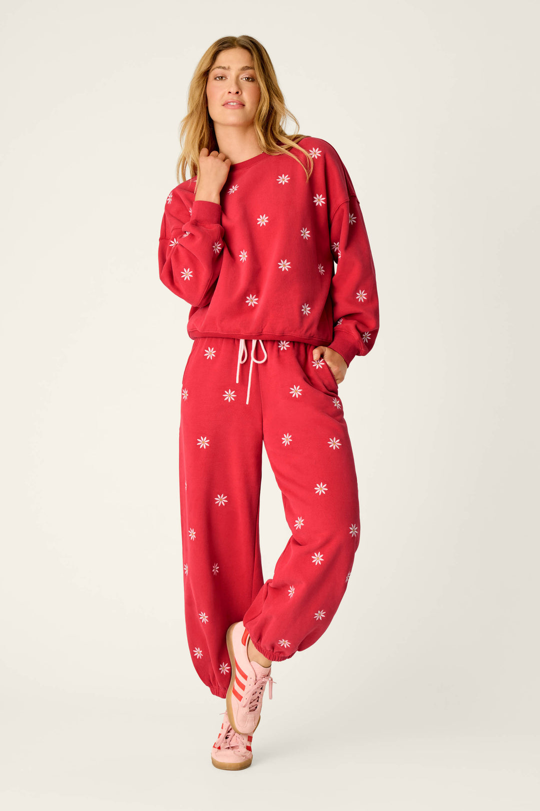 A person wearing the Nature Is My Therapy Embroidered Flowers Frankie Sweatshirt by P.J. Salvage, paired with matching sweatpants and pink sneakers, stands with one hand in their pocket against a plain light background.
