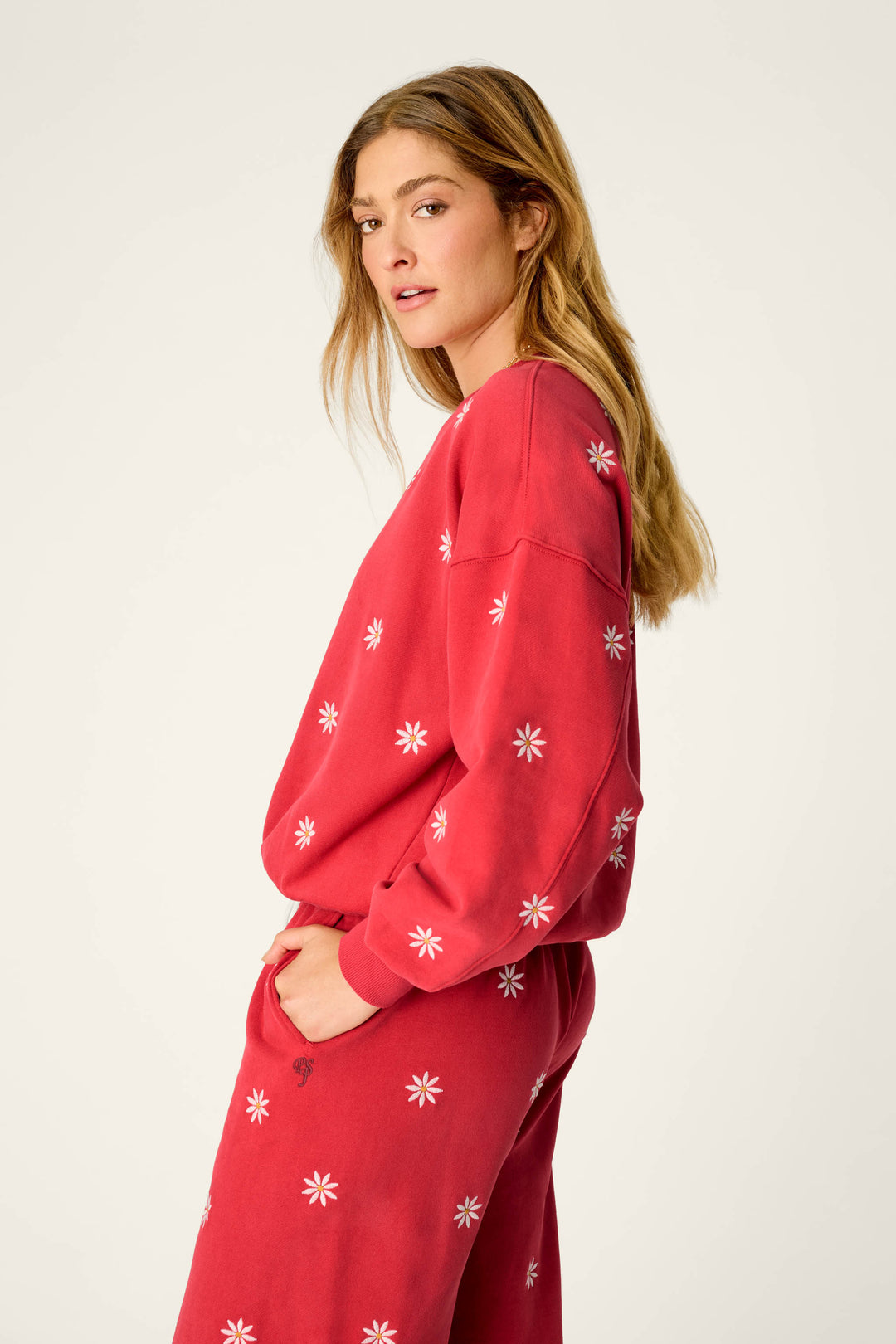 A woman with long blonde hair stands sideways against a plain background, looking toward the camera with one hand in her pocket, wearing the P.J. Salvage Nature Is My Therapy Embroidered Flowers Frankie Sweatshirt and matching pants set adorned with white flower patterns.