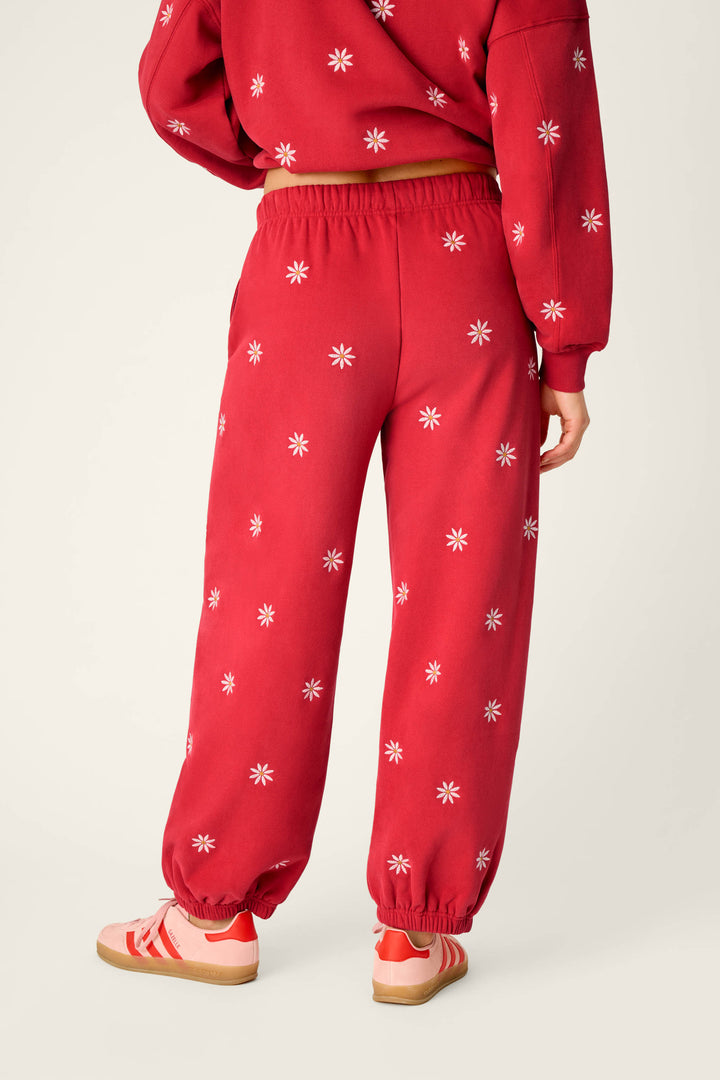 A person is shown from the back against a neutral background wearing the P.J. Salvage Nature Is My Therapy Embroidered Flowers Good Hang Joggers in red, featuring white flower embroidery, paired with a matching sweatshirt and red-striped sneakers.
