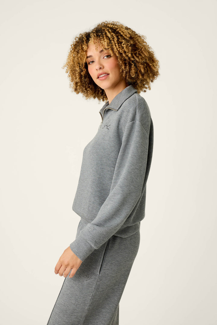 A person with curly hair stands sideways, looking at the camera, wearing the P.J. Salvage Nature Is My Therapy Wish You Were Here Over Night Pullover and matching pants against a plain light background.