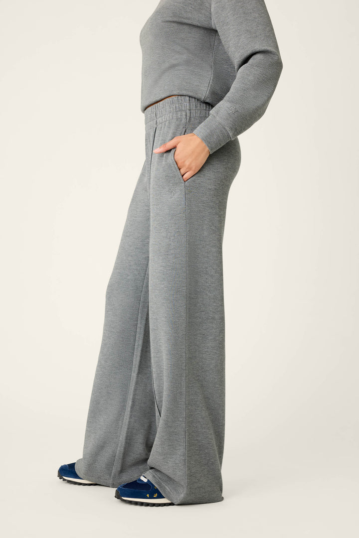 A person wearing P.J. Salvage Nature Is My Therapy Runway Lounge Pants in grey stands sideways with one hand in their pocket. Only their body is visible; they are also wearing navy blue sneakers.