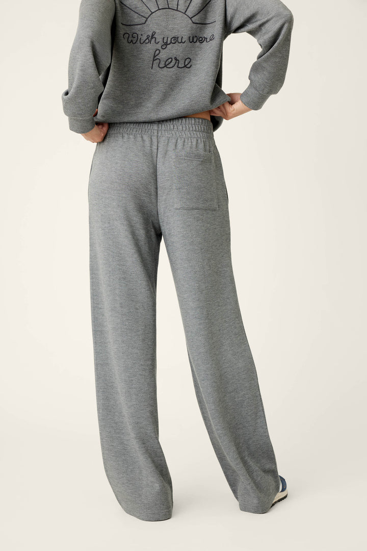 A person stands with hands on hips, facing away from the camera against a plain light background, wearing P.J. Salvage Nature Is My Therapy Runway Lounge Pants and a matching gray sweatshirt featuring writing on the back.