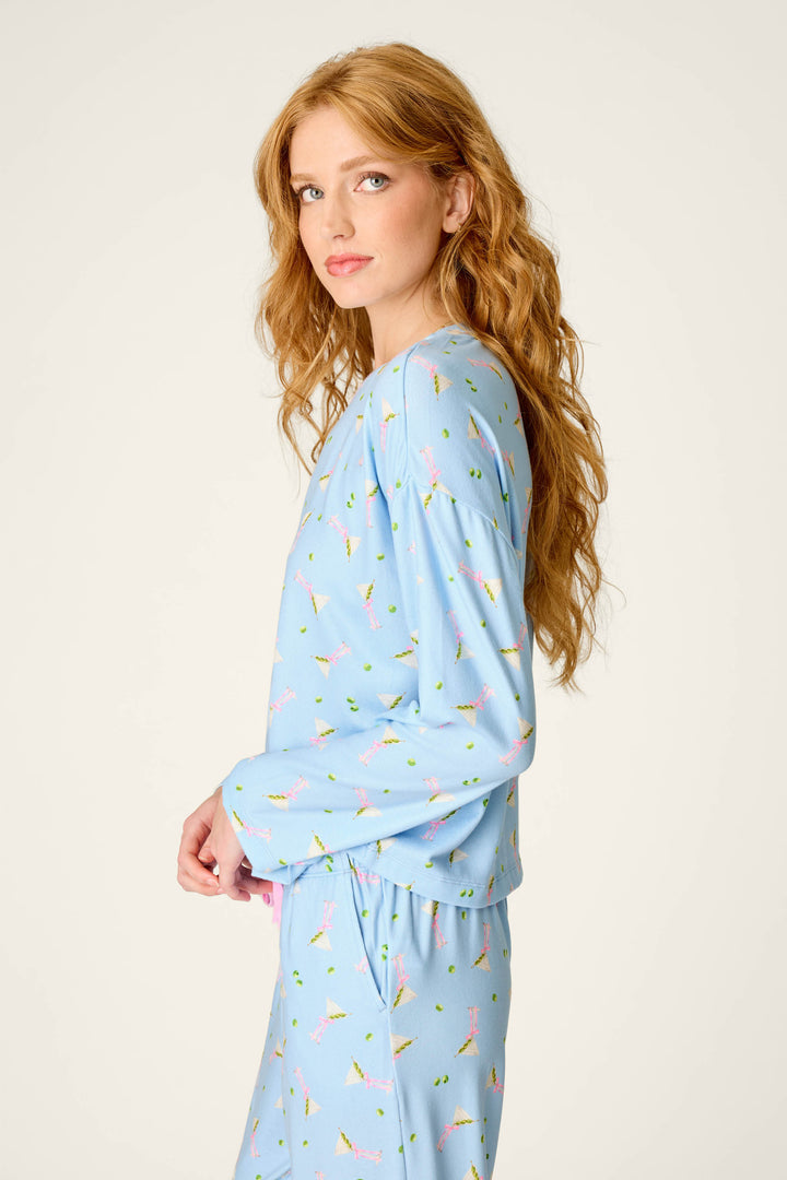 A woman with long, wavy red hair wears the P.J. Salvage Olive You Martini Print Long Sleeve Top, standing against a plain light background and looking toward the camera.
