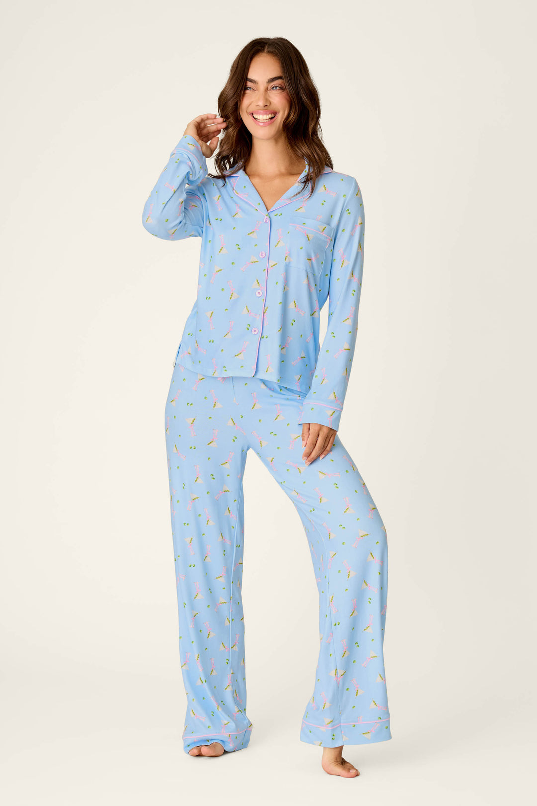 A woman smiles while wearing the Olive You Martini Print Long PJ Set by P.J. Salvage. She stands barefoot against a plain background.