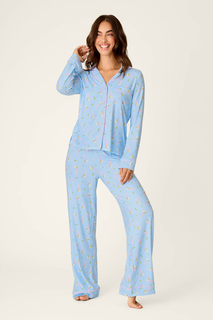 A woman smiles while wearing the Olive You Martini Print Long PJ Set by P.J. Salvage. She stands barefoot against a plain background.
