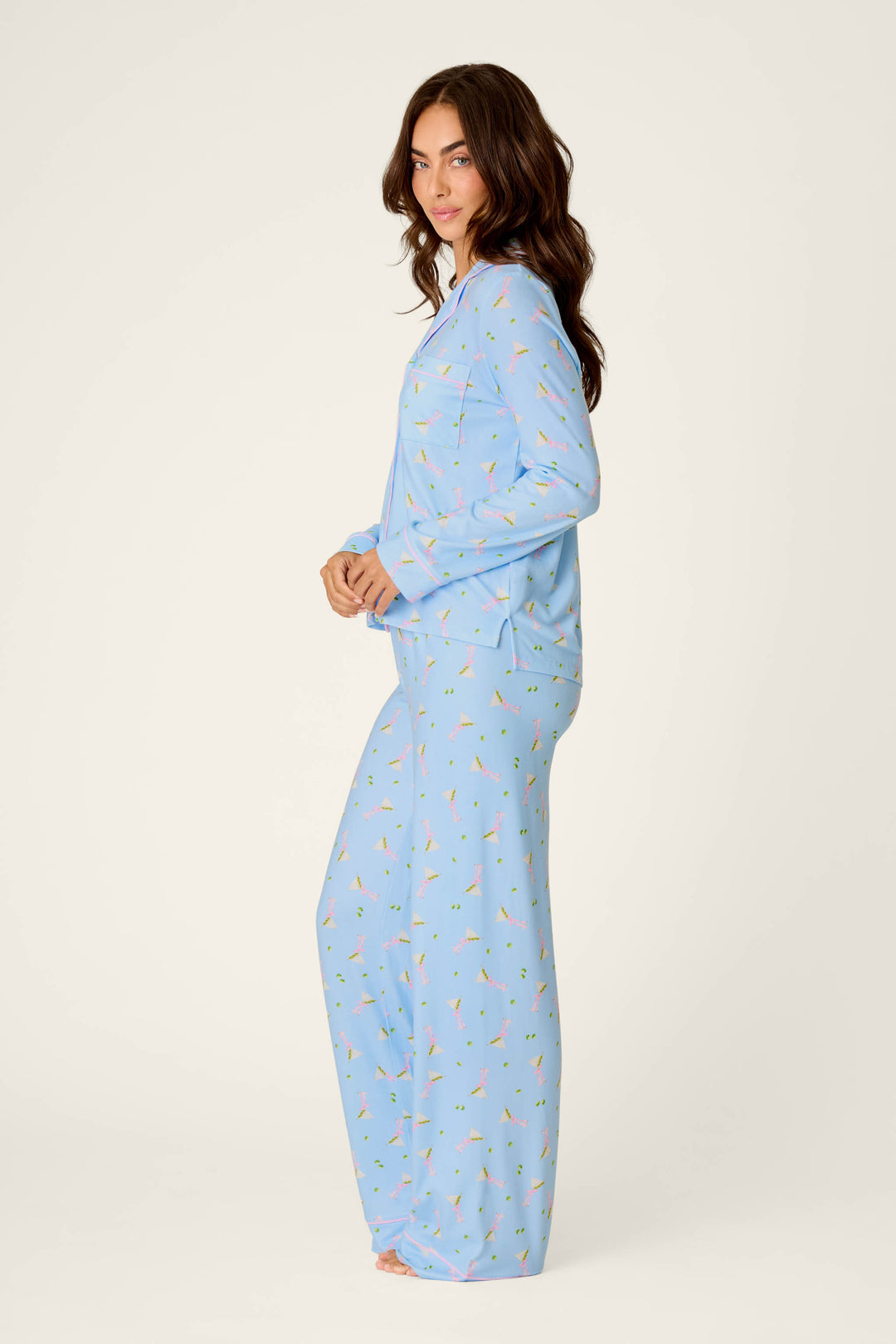 A woman with long brown hair is wearing the P.J. Salvage Olive You Martini Print Long PJ Set, standing barefoot against a plain white background, facing sideways and looking at the camera.