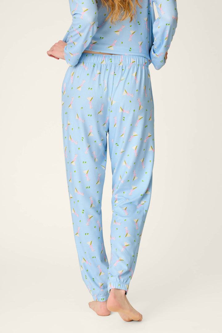 A person is standing barefoot on a white background, facing away from the camera with one arm bent slightly behind their back, wearing P.J. Salvage's Olive You Martini Print Jogger Pajama Pants.
