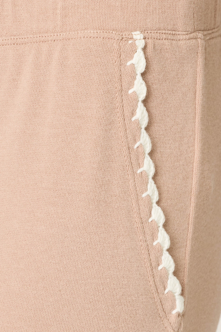 Close-up of the Palms Away Warm Taupe Open Leg Pants by P.J. Salvage, featuring a beige fabric pocket with white scalloped trim along the edge, detailed stitching, and soft knit material.