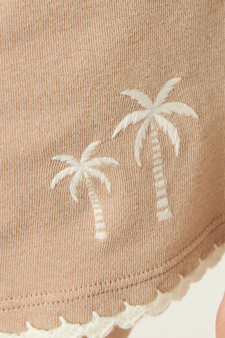 Close-up of P.J. Salvage Palms Away Warm Taupe Shorts featuring light brown fabric with two white embroidered palm trees and scalloped white trim along the edge.