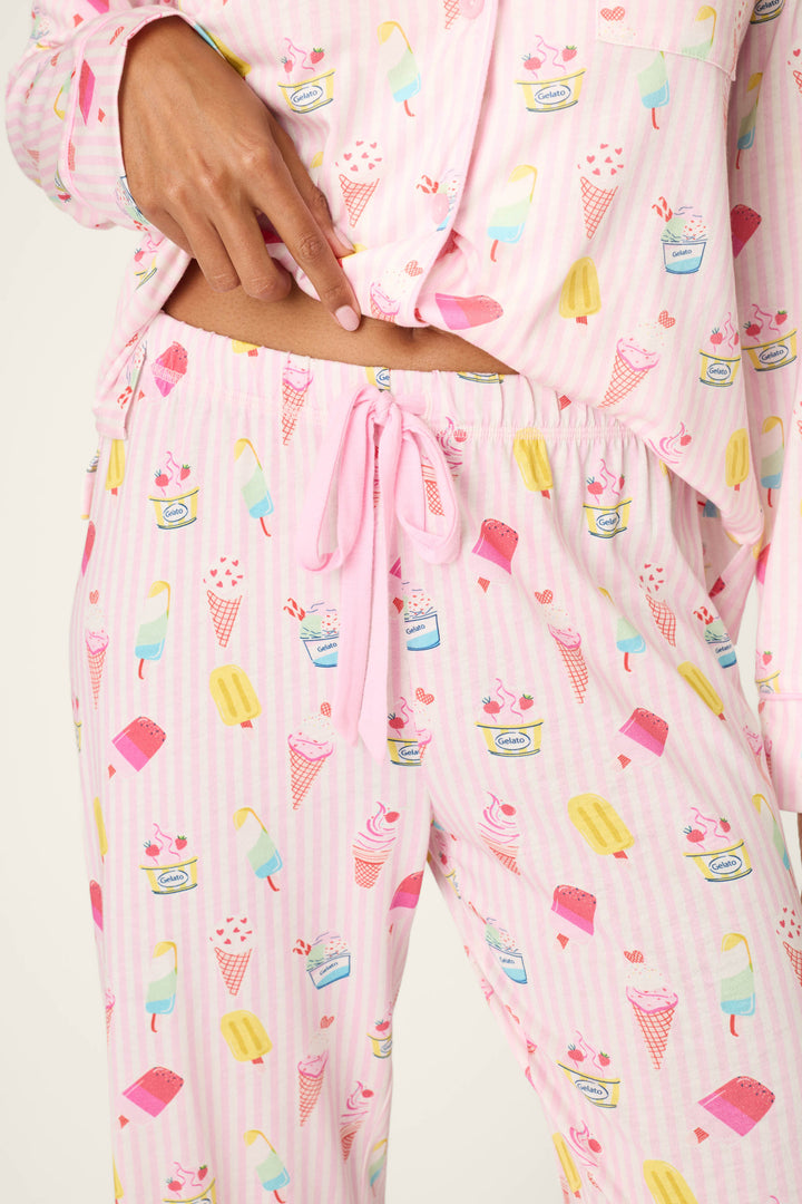 Wearing P.J. Salvage's Playful Prints Sugar Rush Pajama Pants with a colorful dessert-themed print, the person lifts their shirt to reveal the waistband and bow of the fun sleepwear.