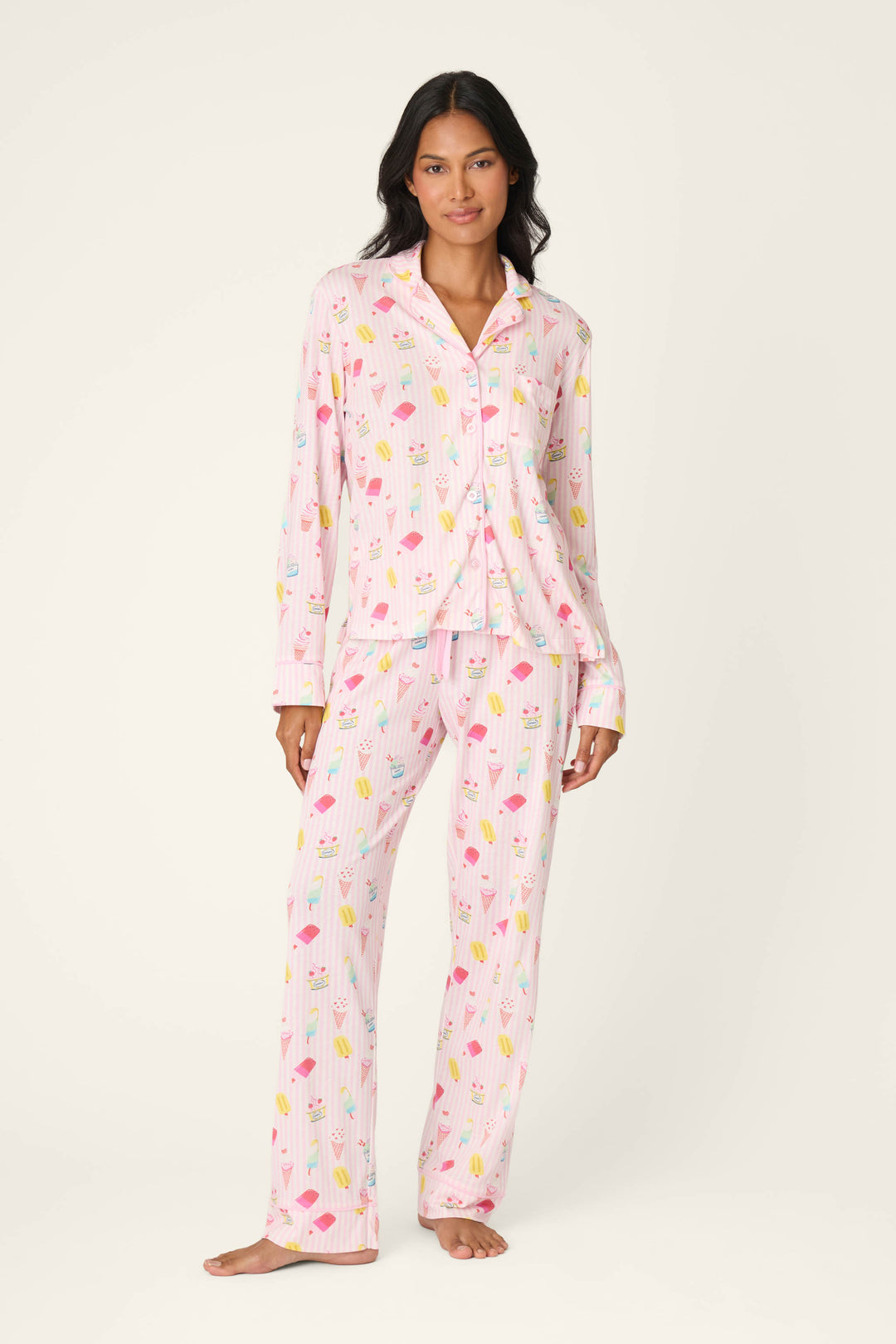 A woman stands barefoot against a plain off-white background, wearing the Playful Prints Sugar Rush Pajama Pants by P.J. Salvage—a pastel pink cotton-modal jersey with a colorful ice cream and popsicle print.