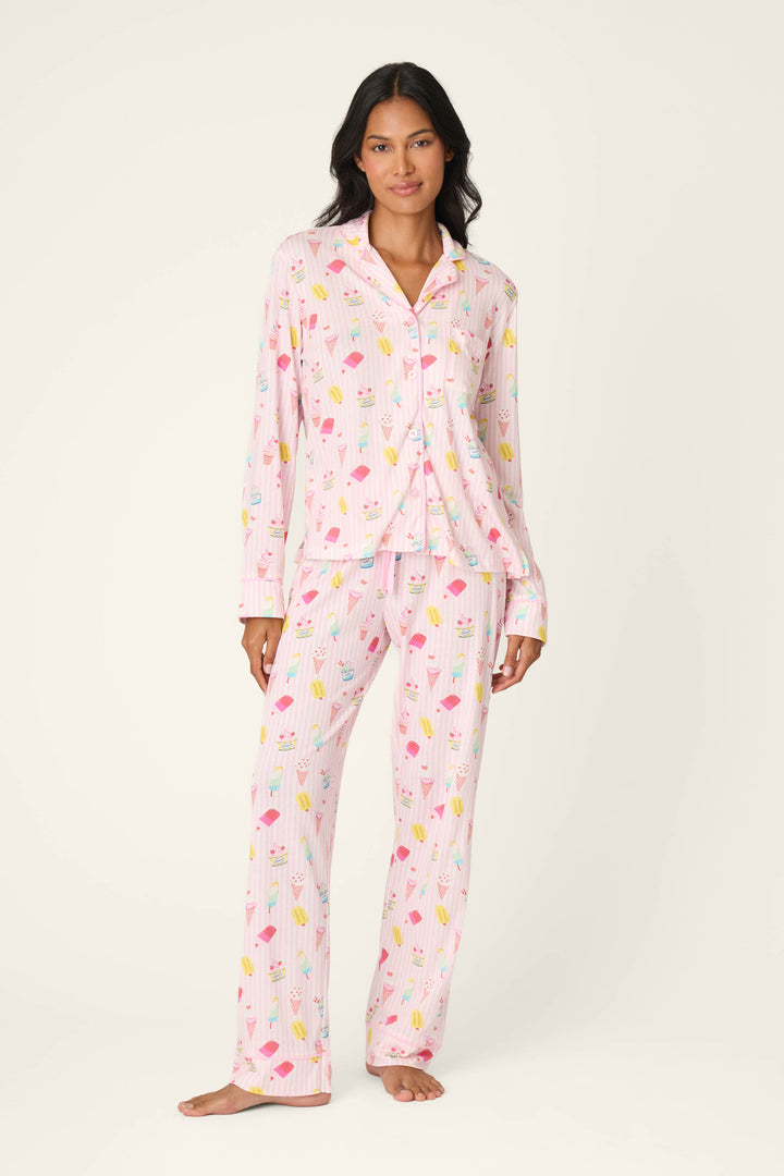 A woman stands barefoot against a plain off-white background, wearing the Playful Prints Sugar Rush Pajama Pants by P.J. Salvage—a pastel pink cotton-modal jersey with a colorful ice cream and popsicle print.
