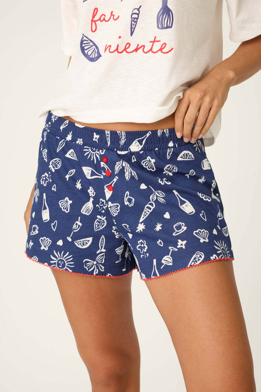 Wearing P.J. Salvage’s Playful Prints Al Fresco Bistro Sleep Shorts—blue with white summer doodles and a red scalloped trim—plus a white tee with red text, perfect for relaxing on the Italian coast in Positano.