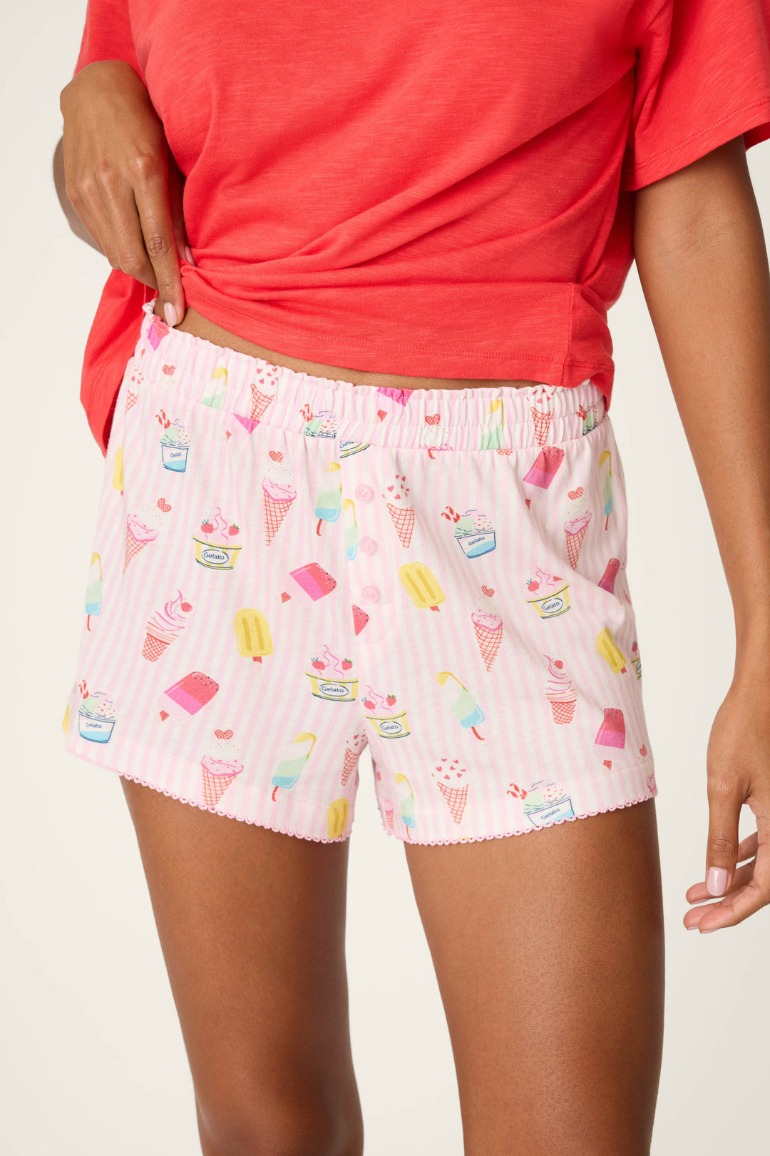 Wearing P.J. Salvage Playful Prints Sugar Rush Sleep Shorts, a person in a red shirt adjusts the waistband of the gelato-print pajama shorts inspired by sweet Amalfi Coast treats.