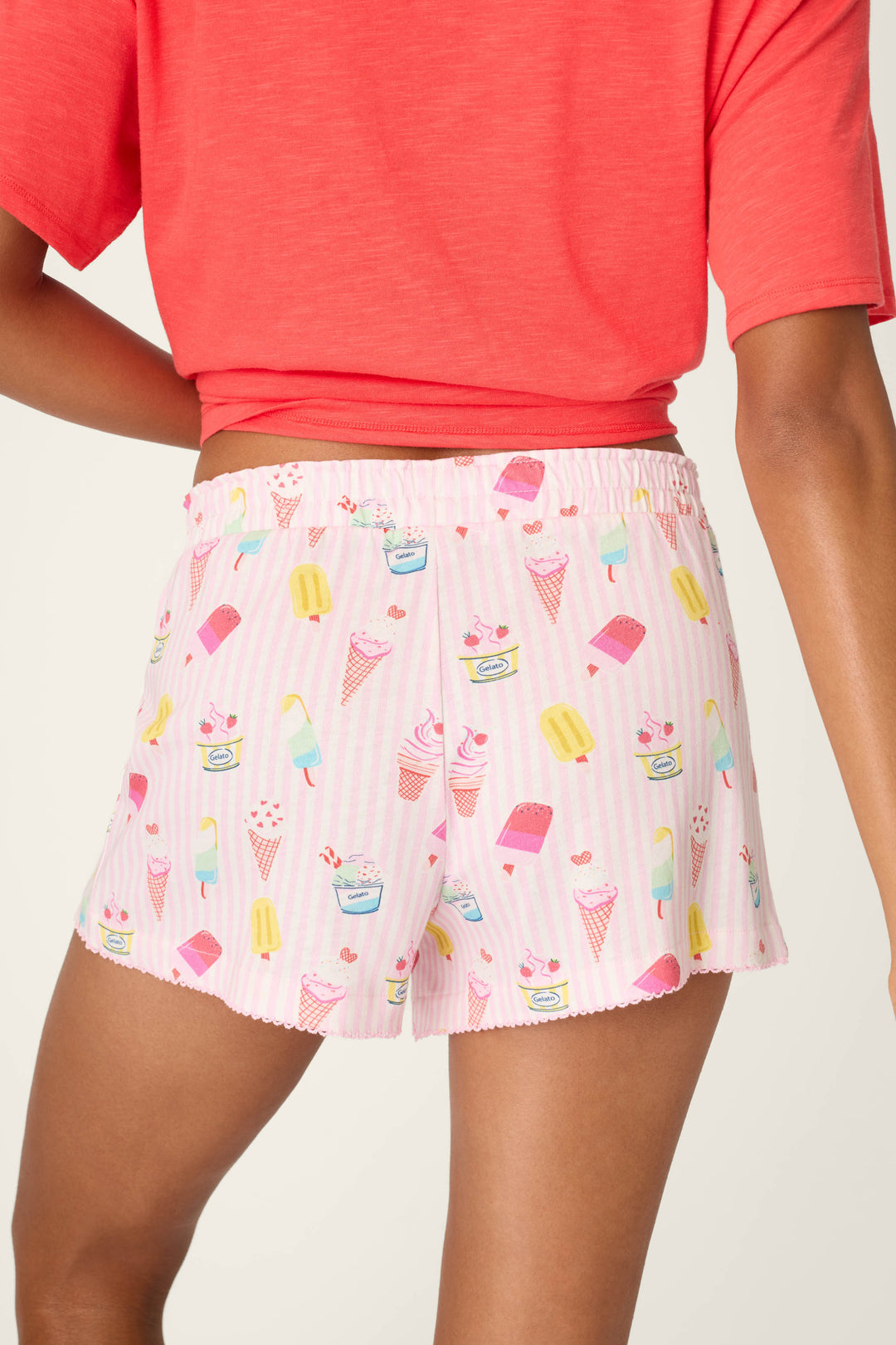 A person stands with their back to the camera, wearing a coral shirt and P.J. Salvage Playful Prints Sugar Rush Sleep Shorts featuring a fun gelato print.