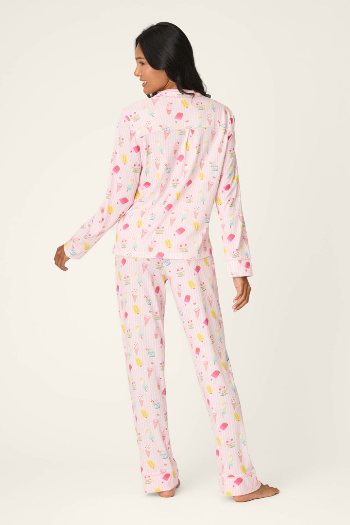 A woman stands barefoot, facing away, wearing the P.J. Salvage Playful Prints Sugar Rush Long PJ Set in light pink with colorful ice cream cones, made from soft cotton-modal jersey, against a plain off-white background.