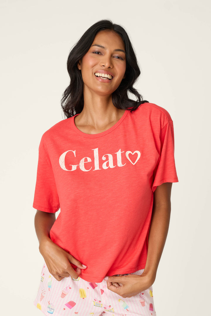 A smiling woman with long dark hair wears the P.J. Salvage Playful Prints Gelato Love Graphic T-Shirt in a relaxed fit and light pajama shorts with a fun pattern, standing against a plain light background.