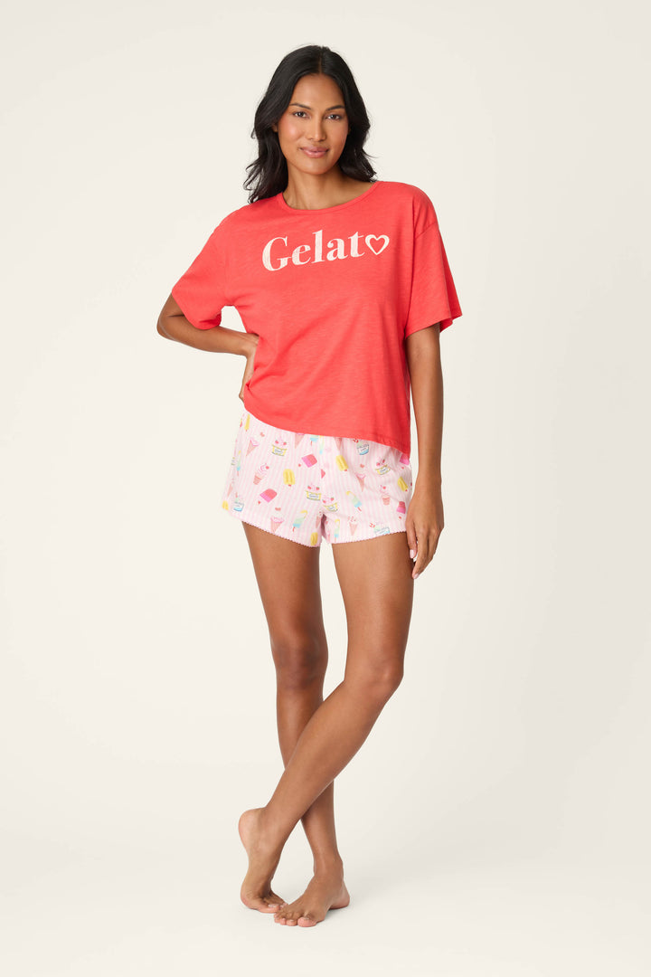 A woman stands barefoot against a light background, smiling with one hand on her hip in a relaxed fit P.J. Salvage Playful Prints Gelato Love Graphic T-Shirt and pink shorts with colorful ice cream prints.