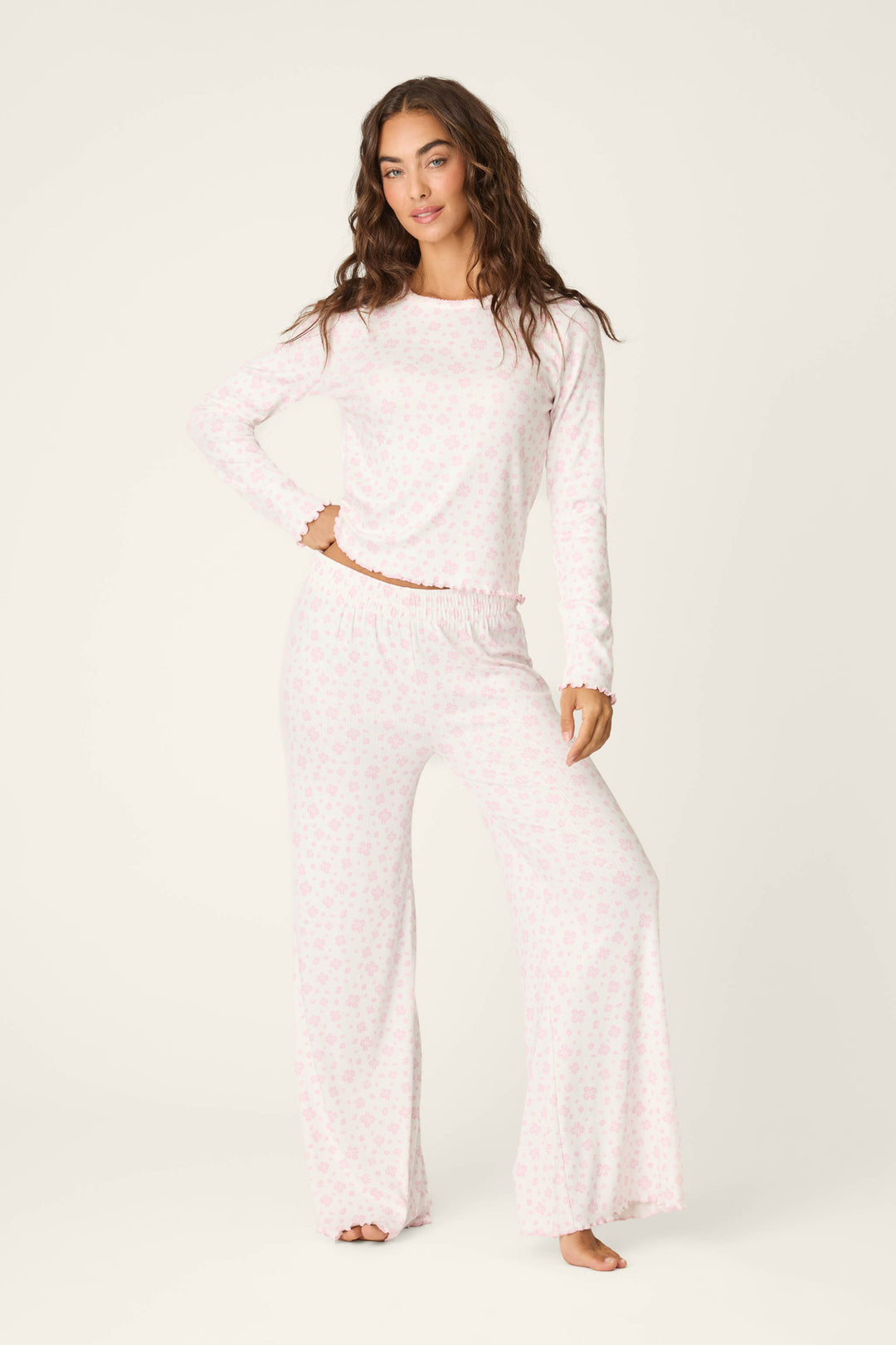A woman stands barefoot against an off-white background, wearing the P.J. Salvage Pretty Petals Sweet Pink Floral Print Long Sleeve Top paired with matching wide-leg pants featuring a subtle floral pattern.