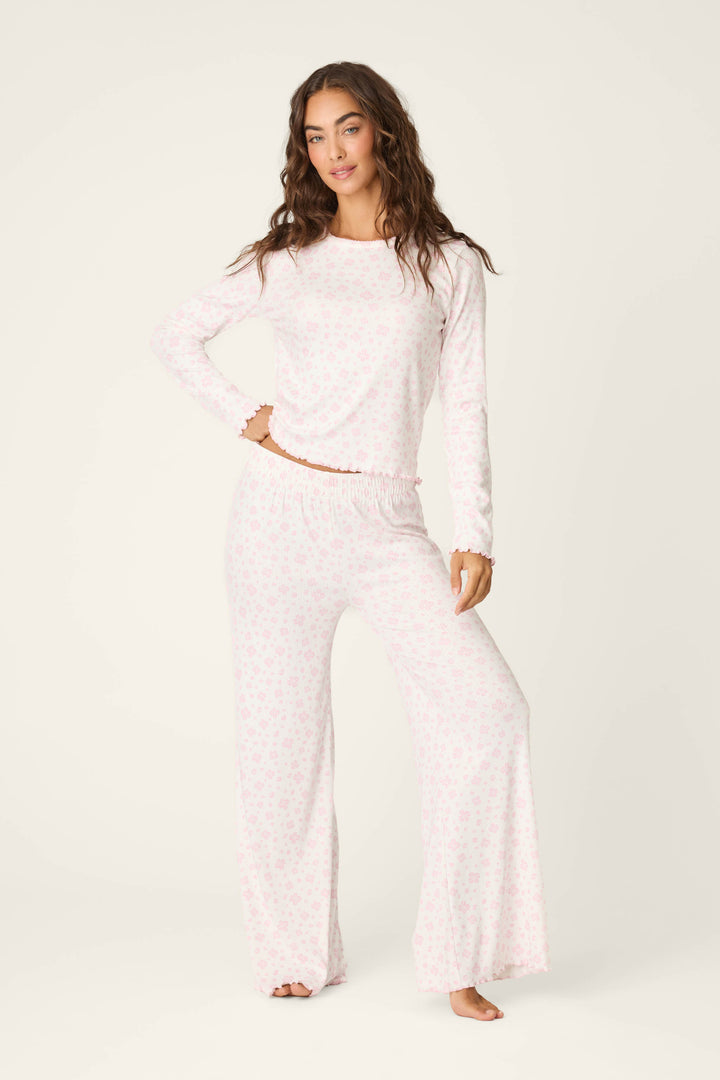 A woman stands barefoot against an off-white background, wearing the P.J. Salvage Pretty Petals Sweet Pink Floral Print Long Sleeve Top paired with matching wide-leg pants featuring a subtle floral pattern.