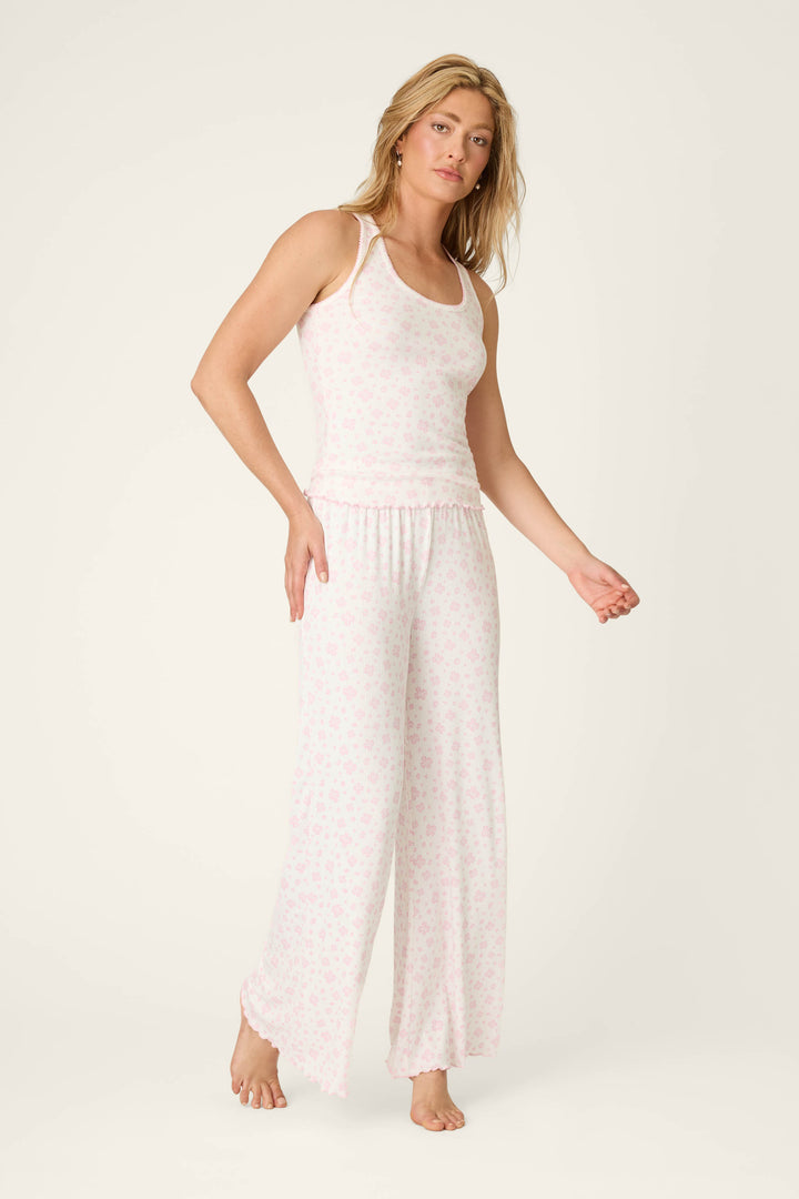 A woman with long blonde hair stands barefoot against a plain background, wearing P.J. Salvage's Pretty Petals Sweet Pink Floral Print Open Leg Pants and a matching tank top.