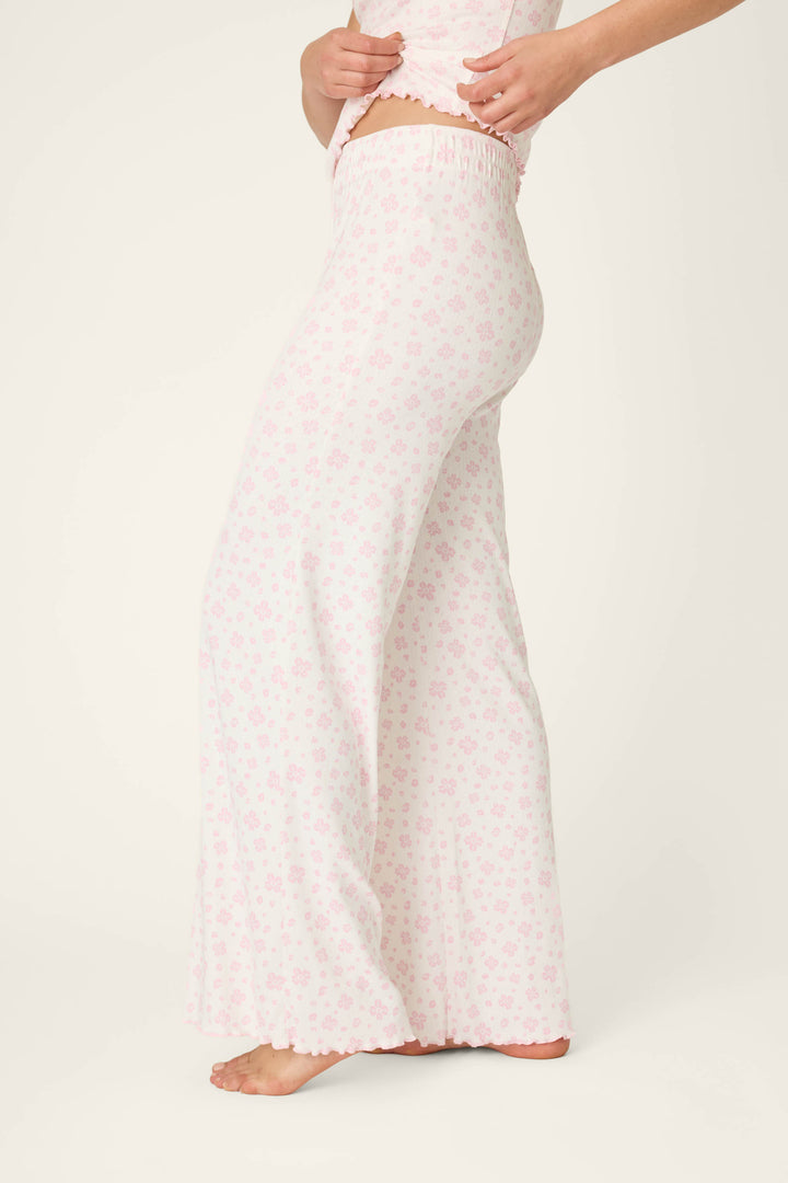 A person stands barefoot, shown from mid-torso to feet in a side view, wearing P.J. Salvage Pretty Petals Sweet Pink Floral Print Open Leg Pants featuring a high waist and wide-leg design with a light pink floral pattern on white.