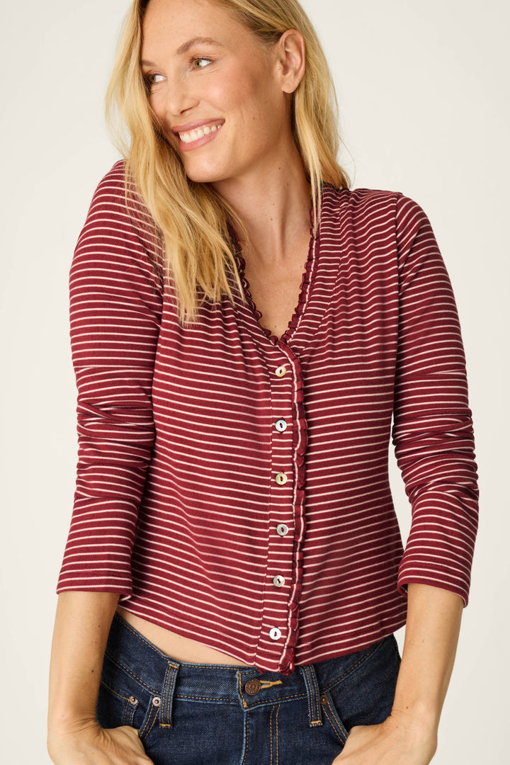 A woman wearing the Pretty Stripes Dark Wine Pointelle Cardigan by P.J. Salvage, smiling and looking to the side, stands against a plain light background.
