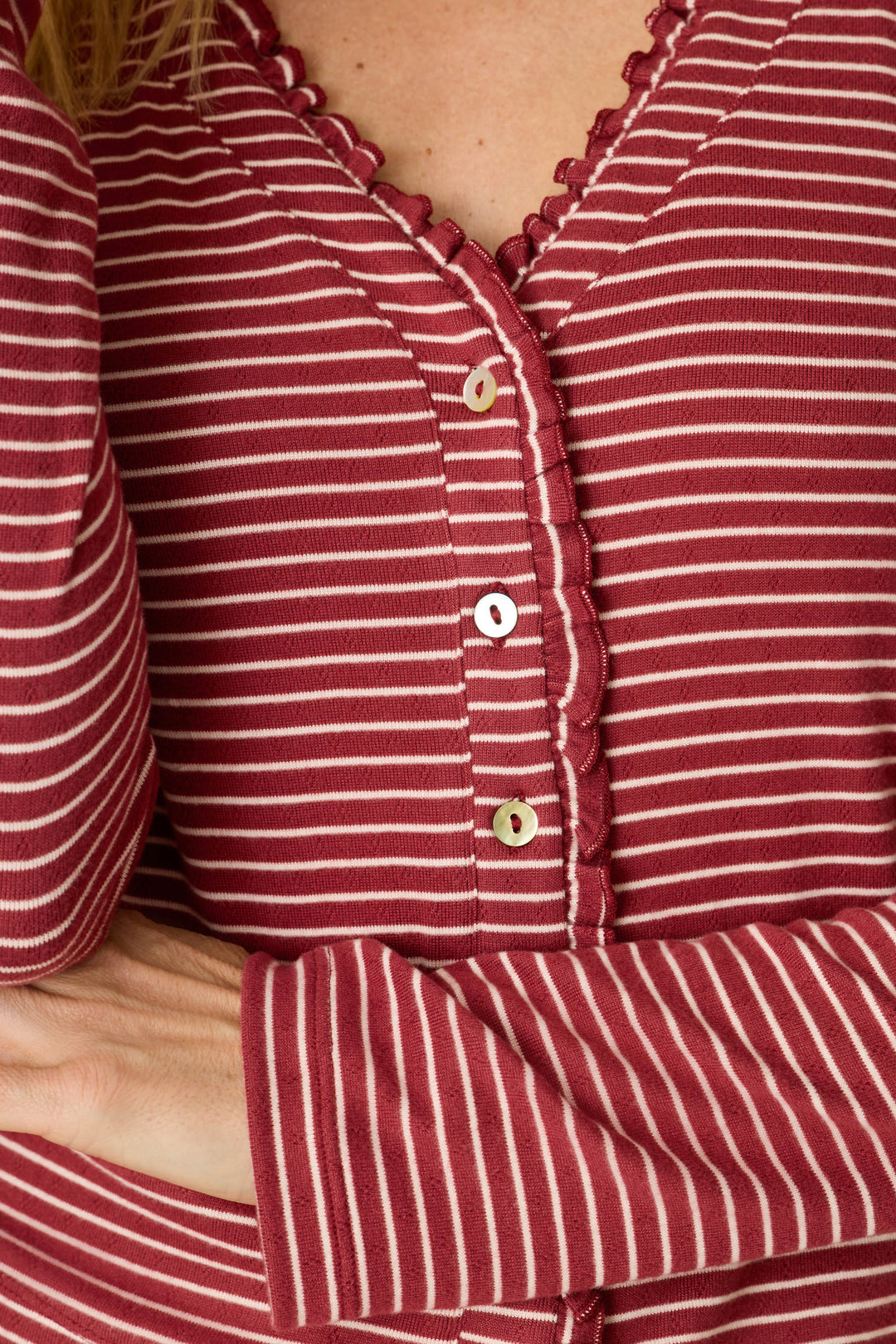 A person wearing the P.J. Salvage Pretty Stripes Dark Wine Pointelle Cardigan, which features red and white stripes with scalloped trim and buttons, is crossing one arm over their body.