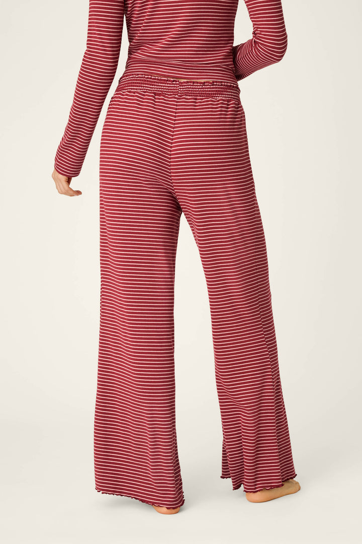 A person stands barefoot with their back to the camera against a plain background, wearing P.J. Salvage’s Pretty Stripes Dark Wine Pointelle Pajama Pants and a matching long-sleeve top.