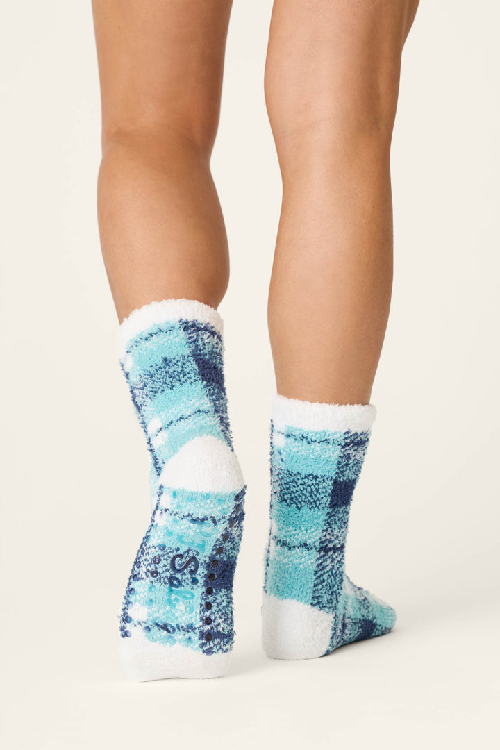 Shown from behind against a plain background, a person stands on tiptoes wearing the P.J. Salvage Plaid About You Blue & Green Plaid Socks, featuring cozy blue and green plaid with letters printed on the bottoms.