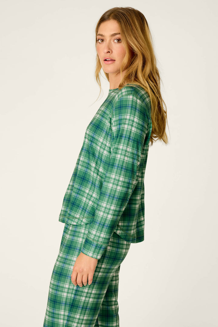 A woman with long blonde hair models the P.J. Salvage Plaid About You Blue & Green Plaid Print Long Sleeve Top, standing sideways and looking toward the camera against a plain light background.