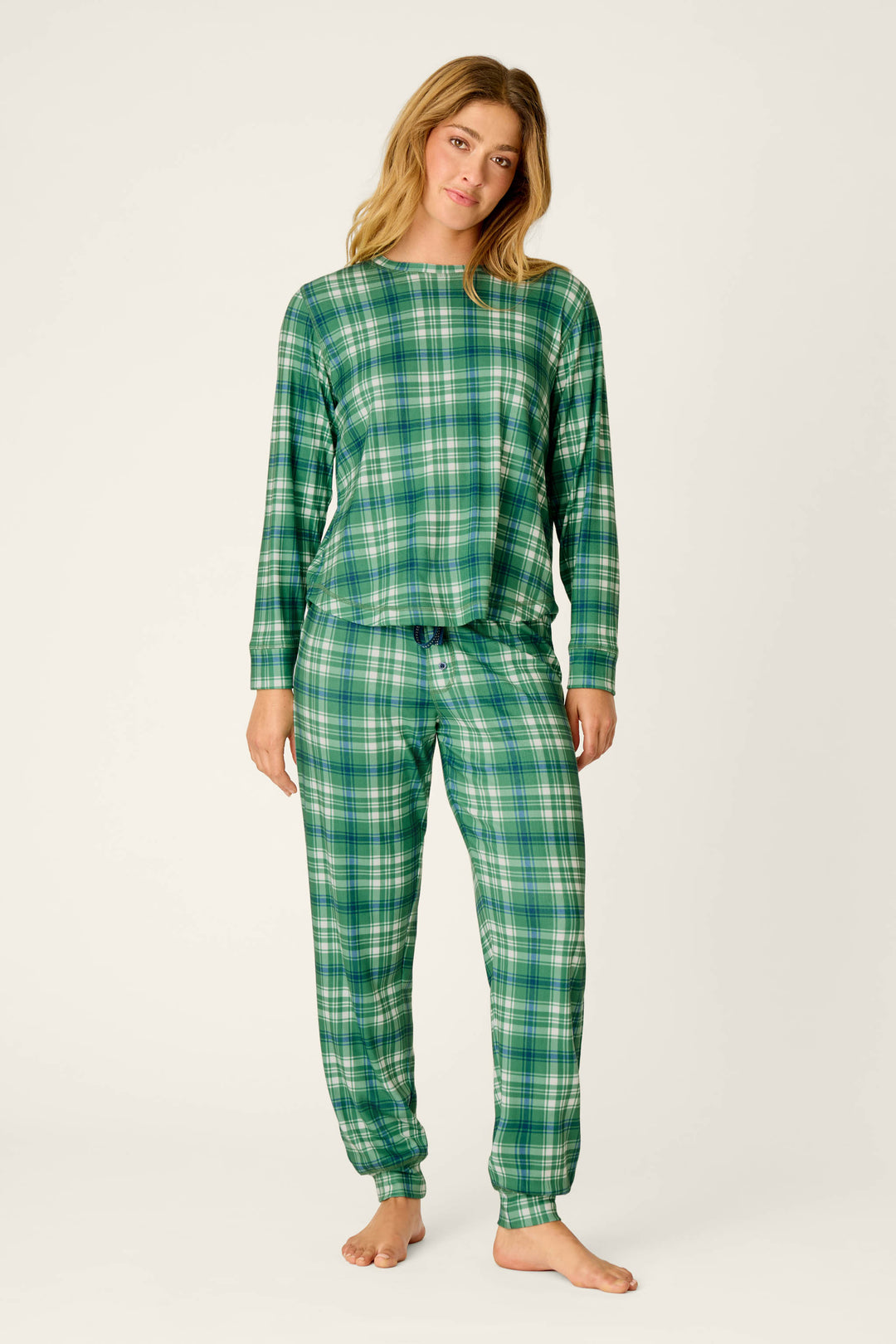 A person stands barefoot, wearing the P.J. Salvage Plaid About You Blue & Green Plaid Print Long Sleeve Top with matching pants, posing against a plain light background.