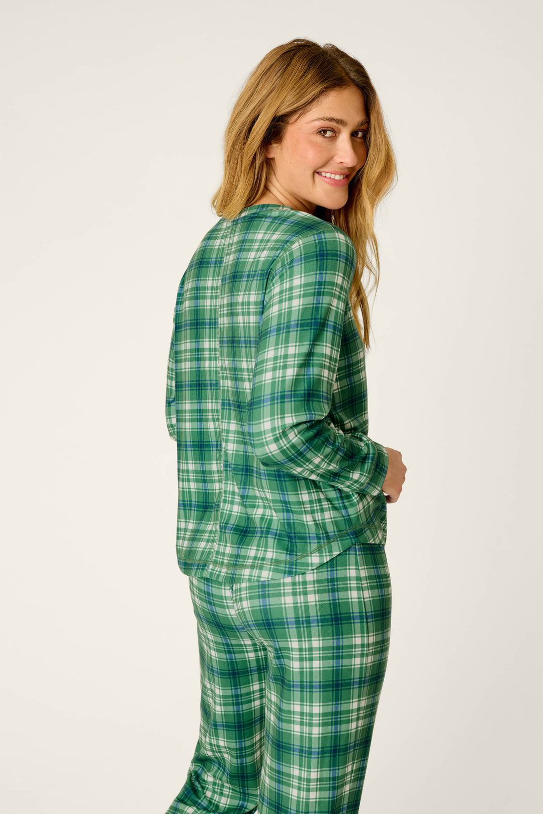 A person with long hair is smiling and looking over their shoulder, wearing the P.J. Salvage Plaid About You Blue & Green Plaid Print Long Sleeve Top, standing against a plain light background.