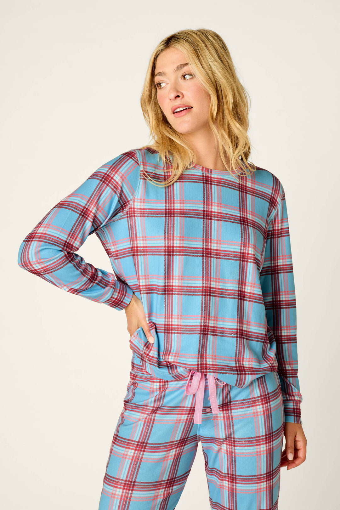 A person is seen standing against a plain light background, looking to the side with one hand in their pocket, while wearing the P.J. Salvage Plaid About You Blue & Red Plaid Print Long Sleeve Top.
