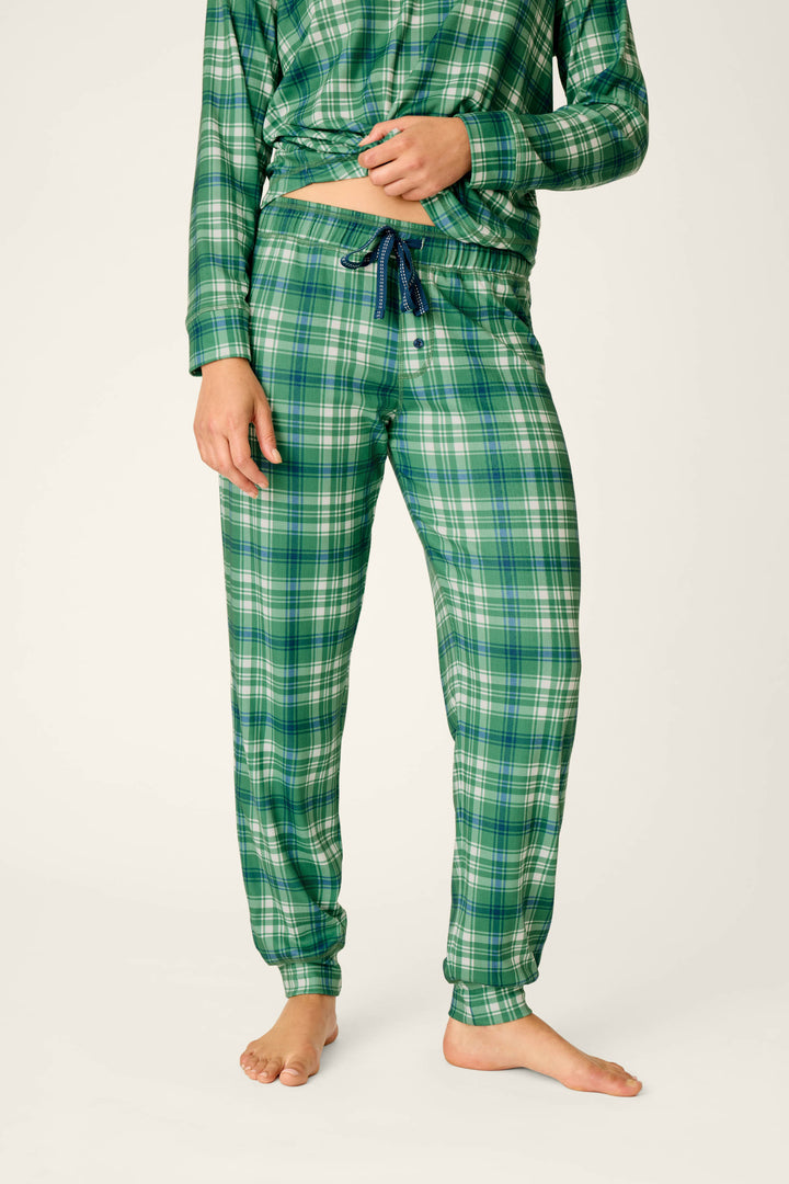 A person is shown barefoot against a plain light background, wearing P.J. Salvage’s Plaid About You Blue & Green Plaid Jogger Pajama Pants, which feature a drawstring waist and relaxed fit. Only the lower body and torso are visible.