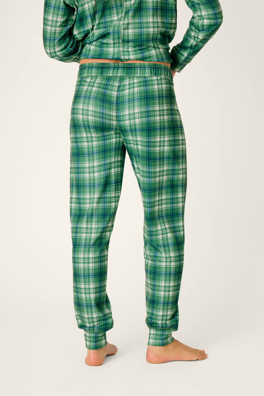 A person stands barefoot, facing away, wearing the P.J. Salvage Plaid About You Blue & Green Plaid Jogger Pajama Pants.