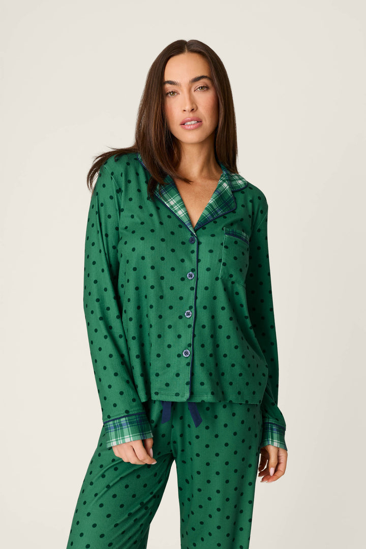 A woman wears the Plaid About You Polka Dots & Plaid PJ Set by P.J. Salvage, featuring green polka dot pajamas with plaid collar and pocket trim, standing against a plain light background and looking at the camera with a relaxed expression.