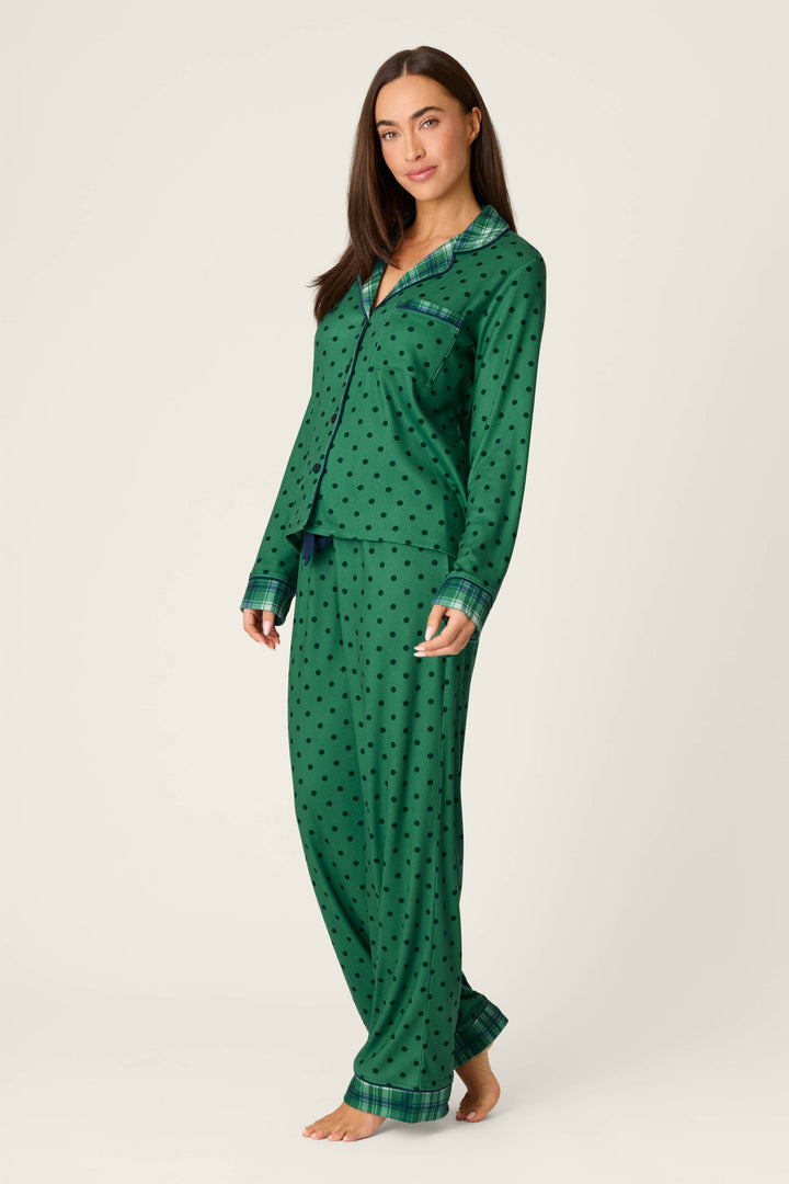 A woman stands barefoot against a plain light background, wearing the P.J. Salvage “Plaid About You Polka Dots & Plaid PJ Set”—a long-sleeve, green polka dot pajama top with matching pants.