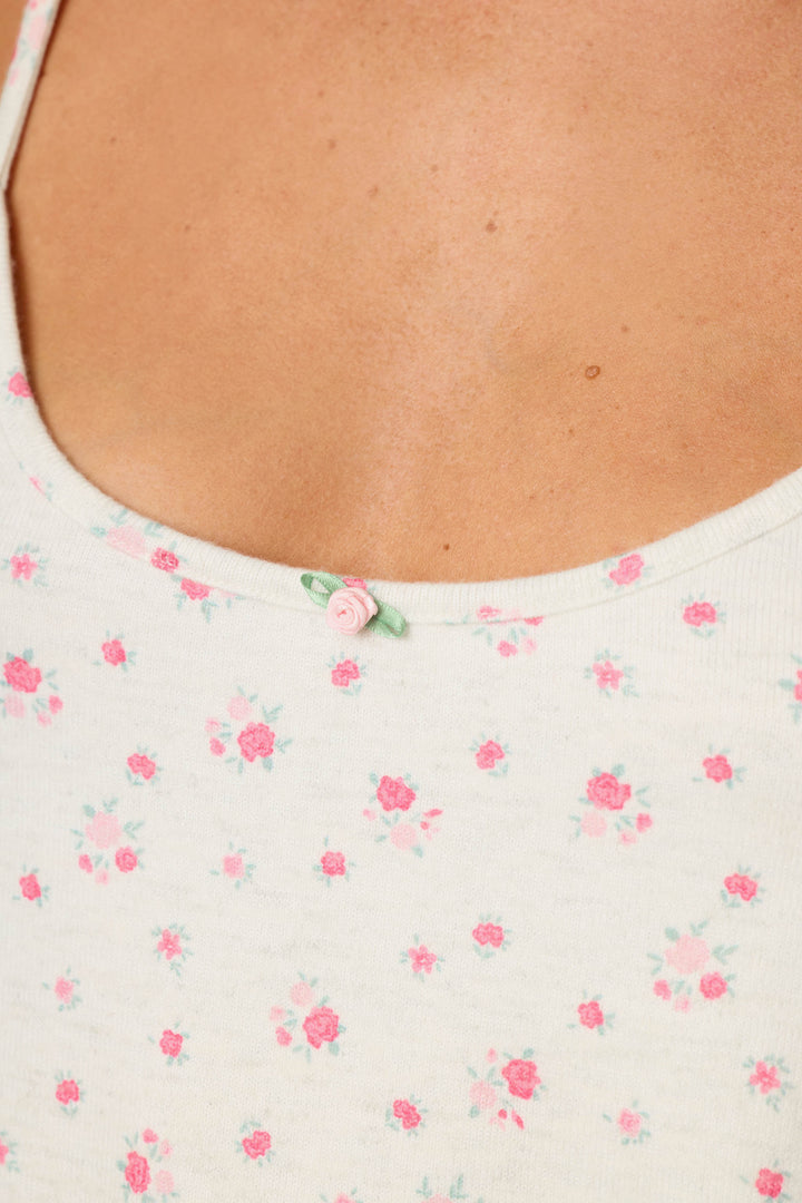 Close-up of a person wearing the P.J. Salvage Romantic Rose Ditsy Rose Print Camisole, a white tank top featuring small pink floral prints and a delicate pink rosette decoration at the neckline.
