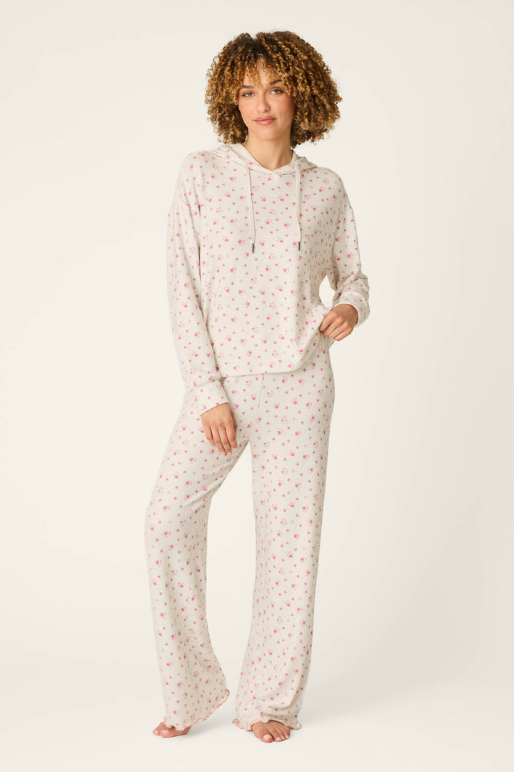 A person stands barefoot, wearing the P.J. Salvage Romantic Rose Ditsy Rose Print Hoodie pajama set, which features a matching hooded long-sleeve top and long pants adorned with a small red floral print on a white background.