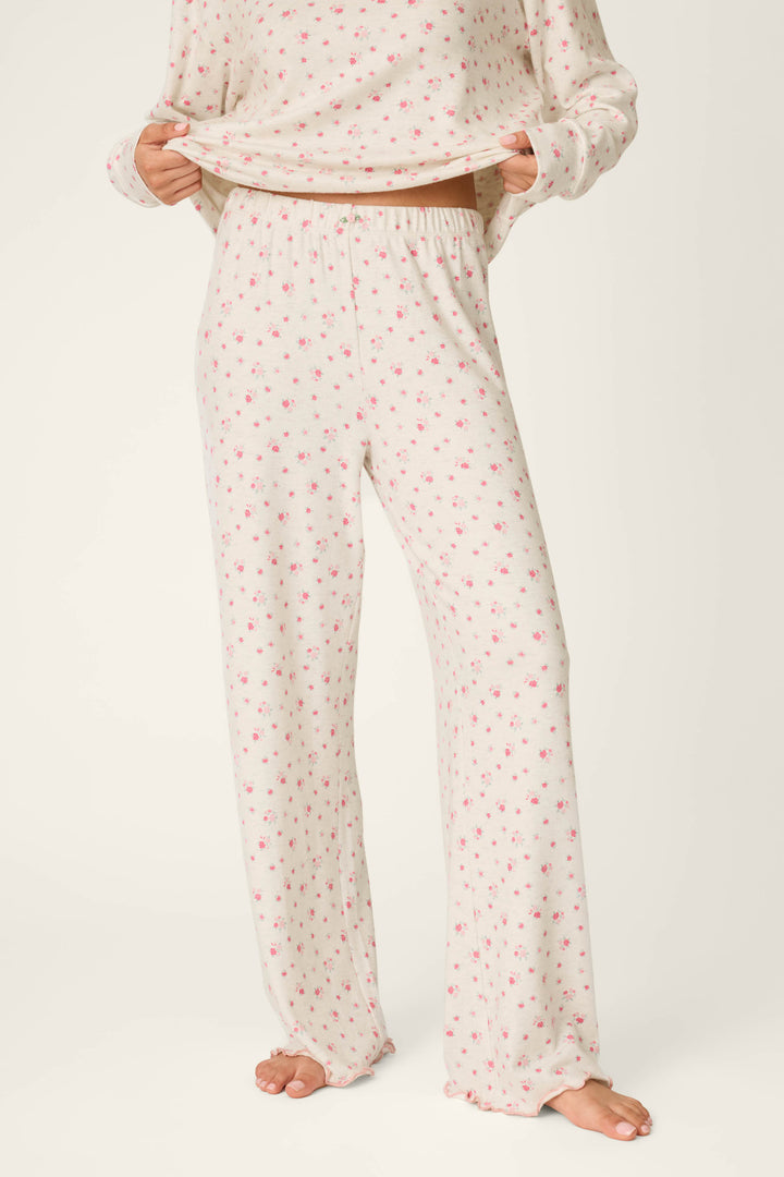 A person is wearing the P.J. Salvage Romantic Rose Ditsy Rose Print Pajama Pants, featuring a cream base with a pink floral pattern, standing barefoot on a light background. The matching pajama top is partially visible and lifted slightly to reveal the waistband.