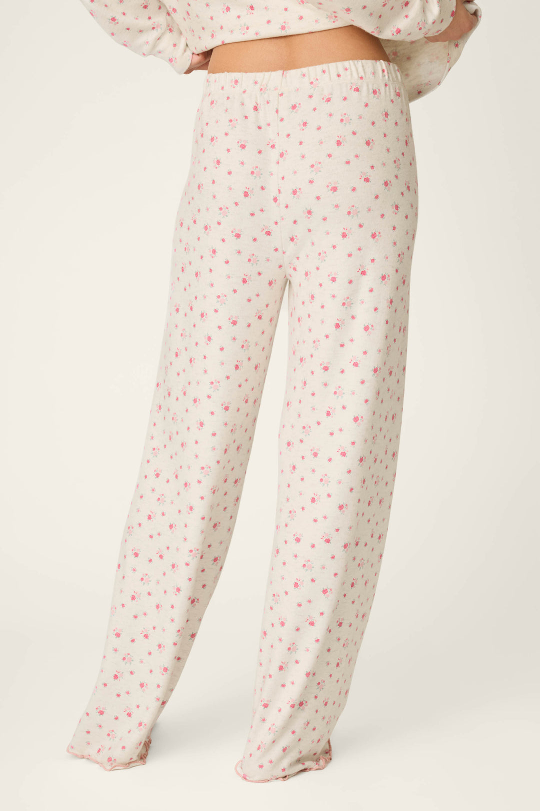 A person is wearing the P.J. Salvage Romantic Rose Ditsy Rose Print Pajama Pants, featuring a pink floral pattern, and is standing with their back to the camera against a plain light background.